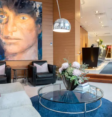 Hotellobby med stor tavla föreställande ansikte, soffor, fåtöljer och receptionsdisk
