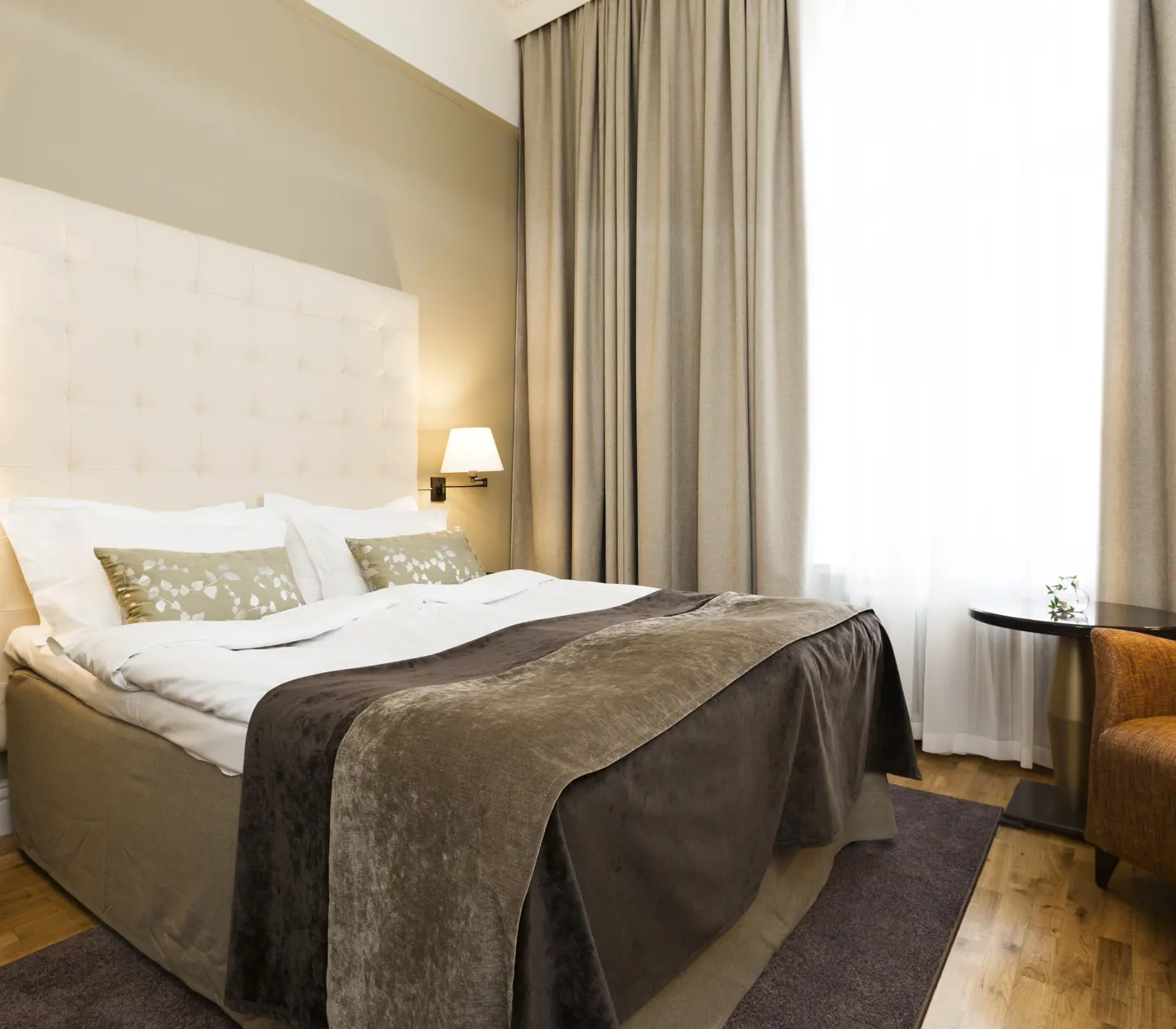 Bright hotel room with bed, white headboard and armchair